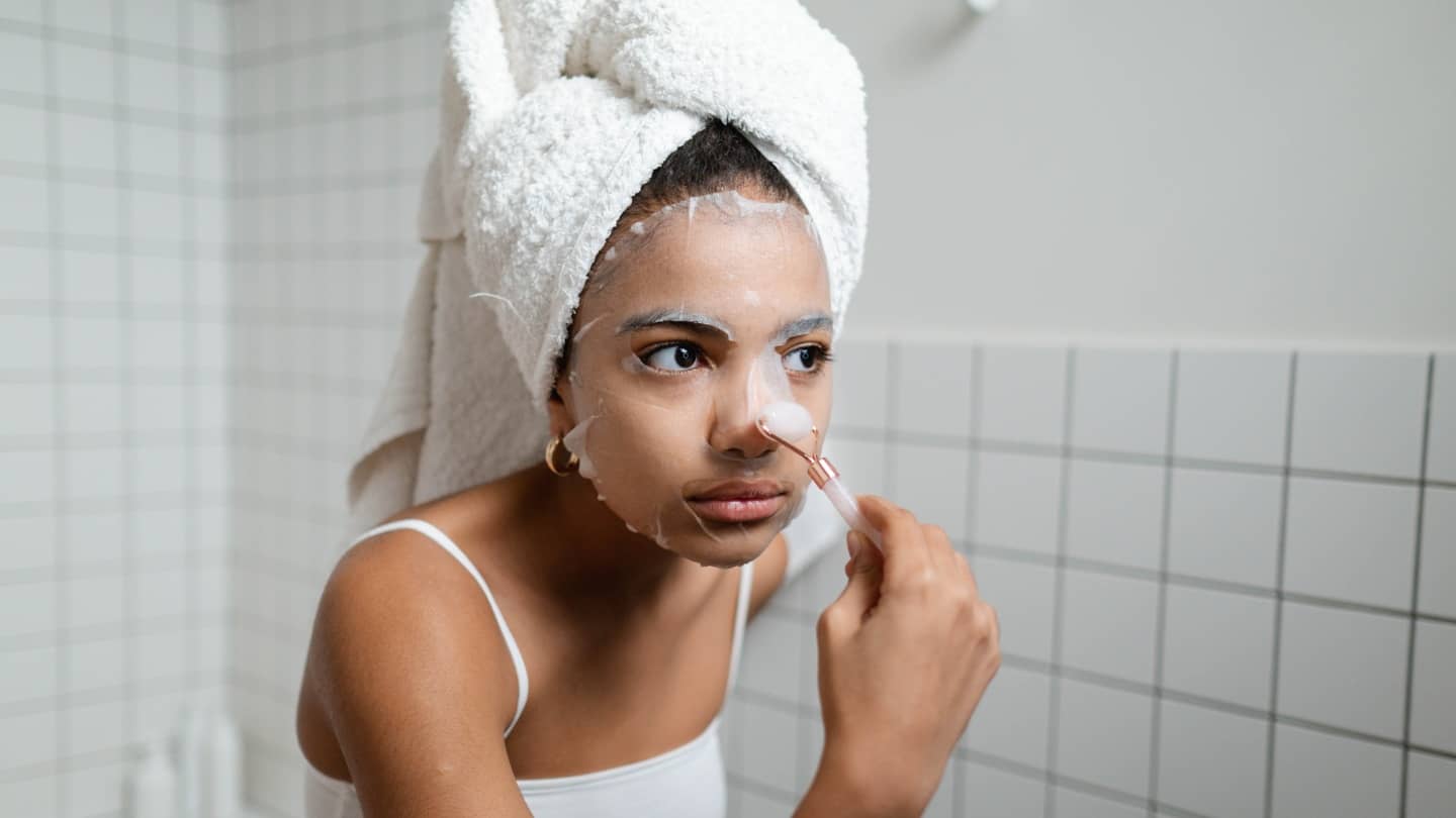 woman using jade roller and face mask to prevent acne and clear her skin