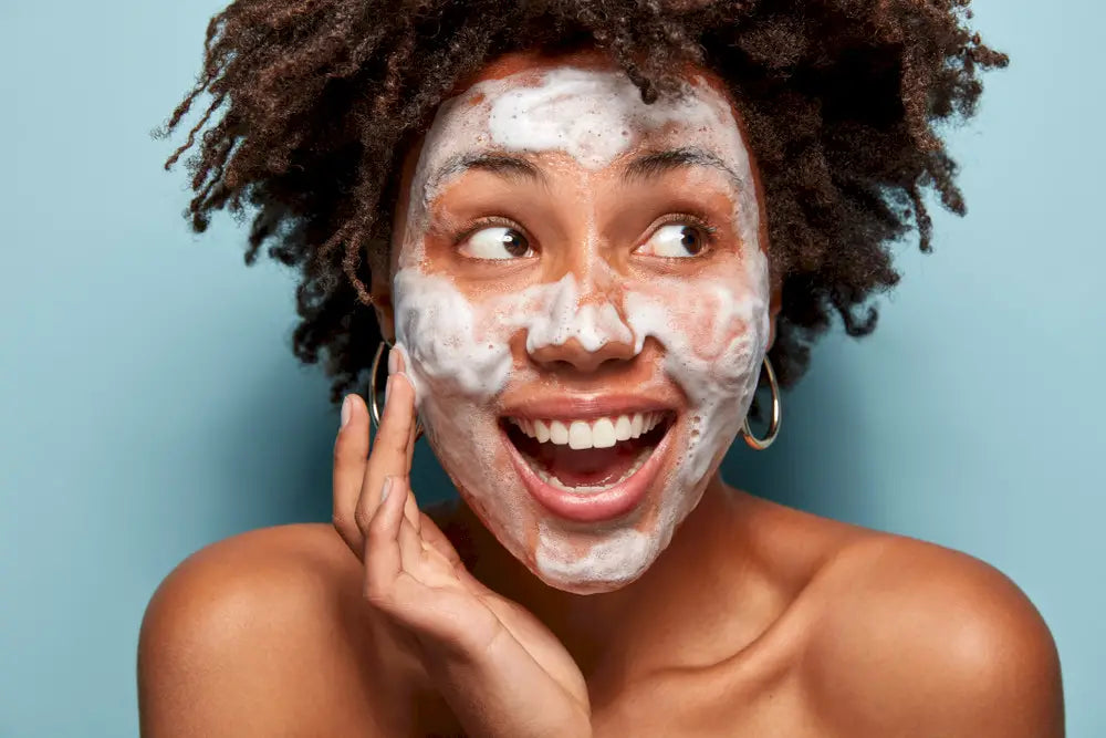 Woman smiling at camera with foaming cleanser on face