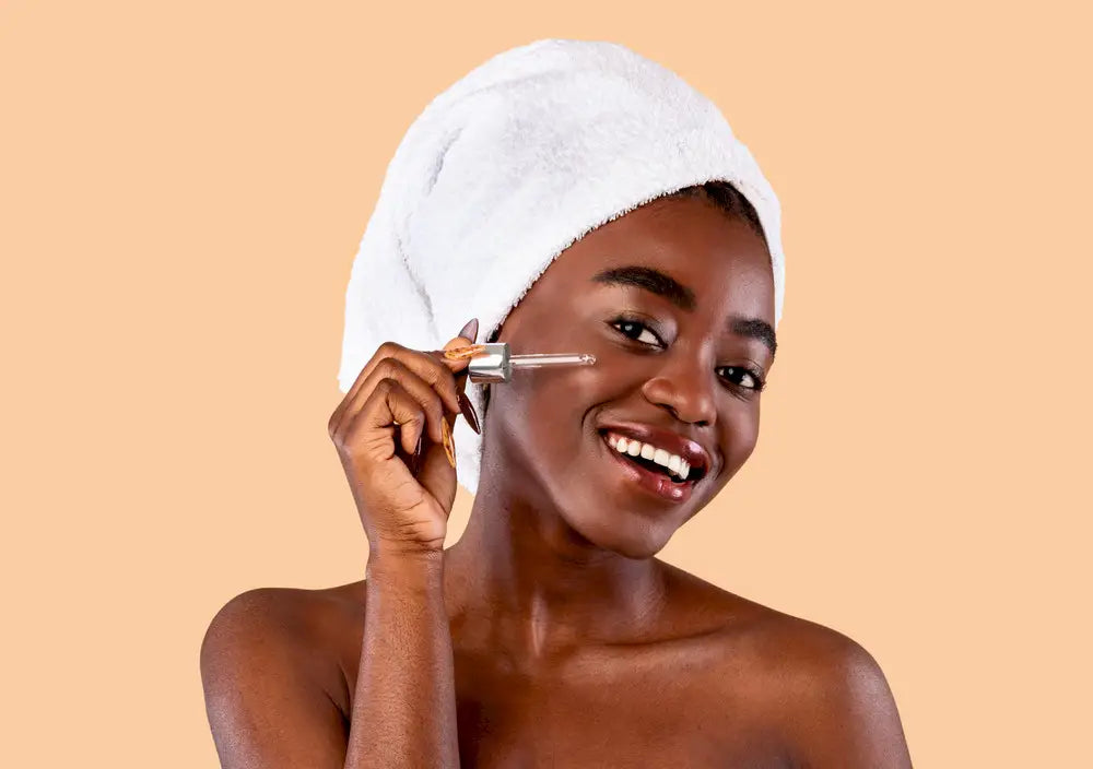 Smiling woman with towel on head applying retinol serum with a dropper