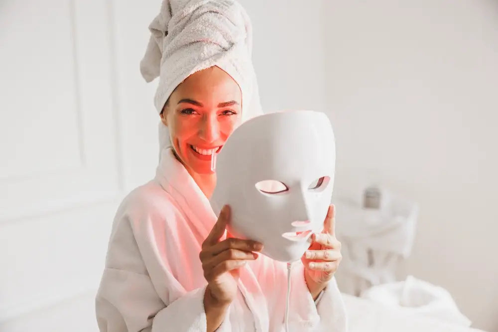 Woman smiles while holding a red LED light therapy mask