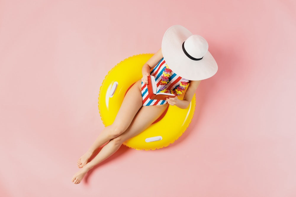 Woman lounging in bathing suit on pool float on pink background