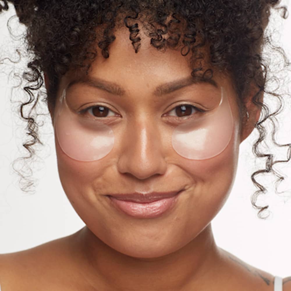 Woman with curly hair wearing clear under-eye gel patches, highlighting hydrated and refreshed under-eye skincare results