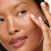 Close-up of a woman applying cream-colored whipped gel cream to her cheek, with her fingers touching her face. White text on the right reads 'ultra-plush whipped gel cream'.