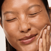 Close-up of a woman's face with closed eyes and a hand touching her cheek, showing a smooth, dewy complexion. White text on the right reads 'ultra-fine mineral micro-mist'.