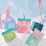 Six eye gel packets arranged on white snow with pink skis and a snowy outdoor background. The packets are in different colors: blue, green, pink, and teal, with the central packet reading 'PATCHING ALL THE WAY'.