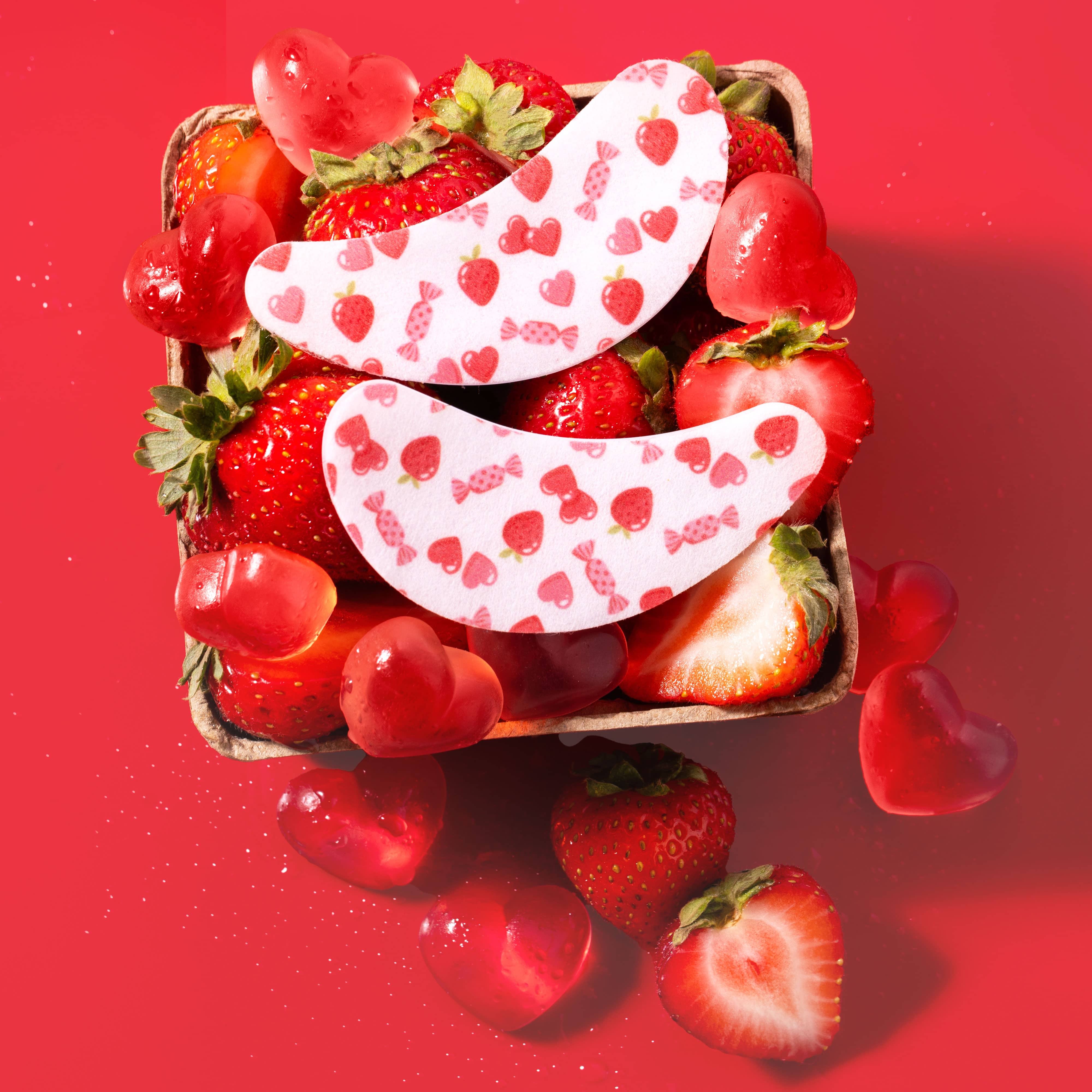 Strawberries and heart-shaped candies with eye patches on a red background