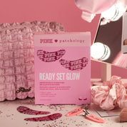 Ready Set Glow smoothing eye patches box with burgundy patches, a pink satin scrunchie, hair clips, and a quilted bag