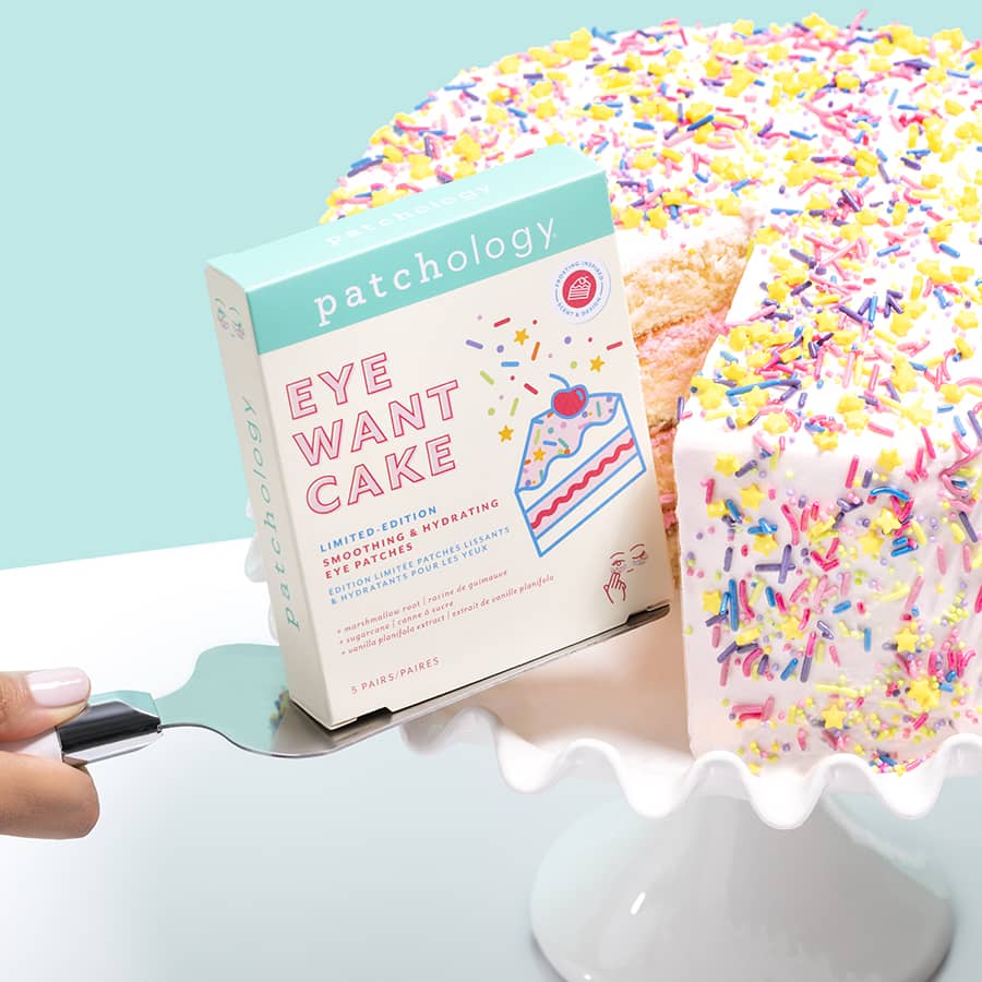 Patchology Eye Want Cake eye patches box beside a sprinkle-covered cake slice on a stand, highlighting a playful, dessert-inspired brightening and hydrating under-eye treatment
