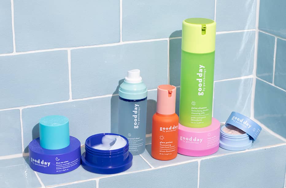 A collection of Good Day skincare products in various colorful containers, arranged on a light blue tiled surface.