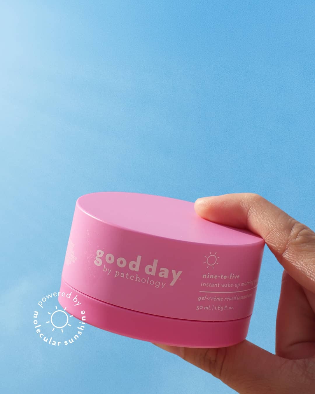 A hand holding a pink cosmetic jar labeled 'good day' nine-to-five morning moisturizer against a solid blue background.