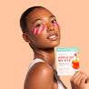 Woman wearing exclusive Sprinkles apple of my eye under-eye patches with a product packaging on a beige background