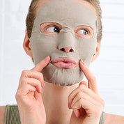 Person applying a Detox Smartmud facial mask on a white background