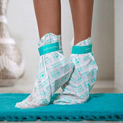 Feet wearing Patchology foot mask booties with teal label, standing on mat for hydrating foot care treatmen