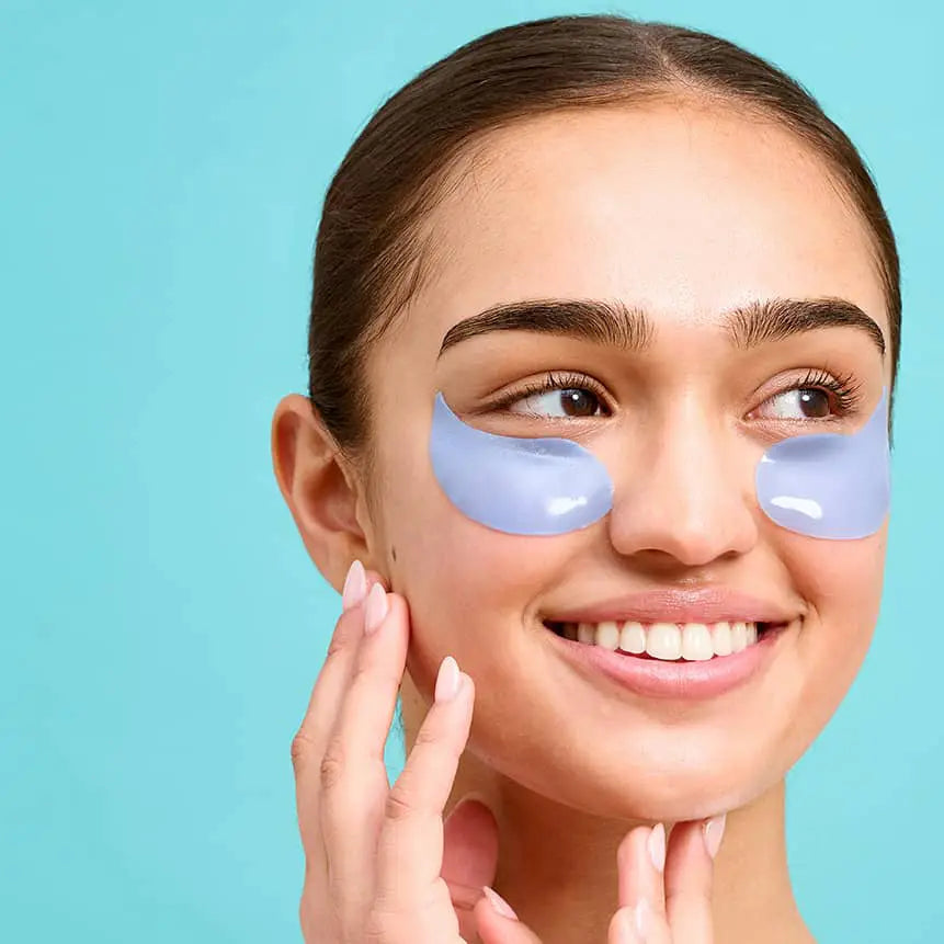 Smiling woman wearing blue hydrogel under-eye patches, brightening and hydrating eye skincare treatment
