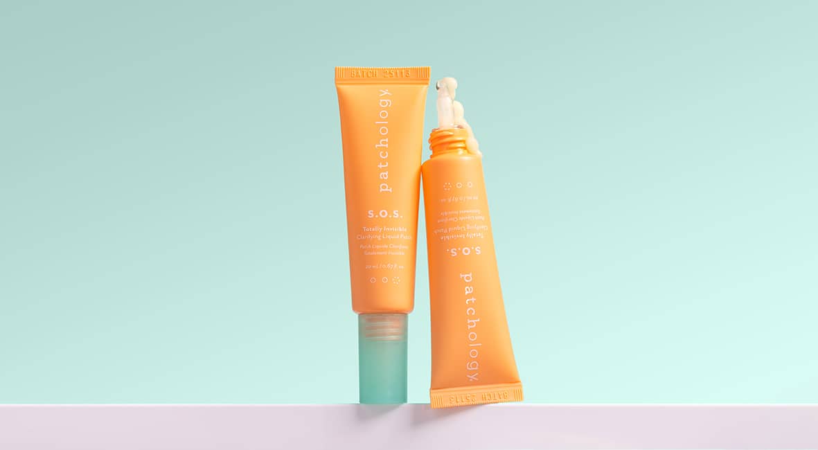 Two orange SOS tubes of sunscreen on a light blue and pink gradient background