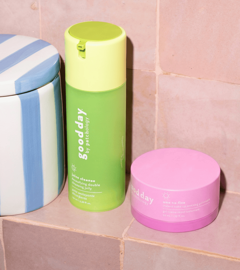 Two Good Day juice cleanse double facial cleanser and nine-to-five skincare products on a pink tiled surface: a green and yellow pump bottle labeled 'deep cleanse' and a pink jar labeled 'time to relax'.