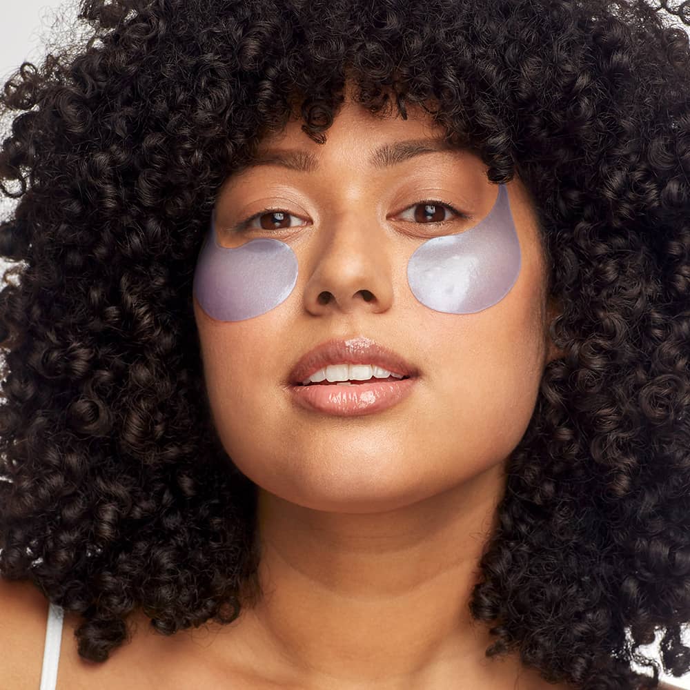 woman with dark brown curly hair wearing restoring eye gels