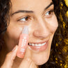 Woman with curly brown hair applying moisturizing roll on eye serum